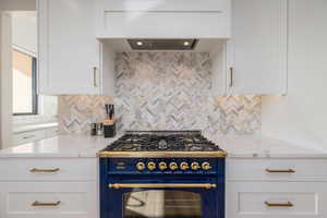 Kitchen with backsplash, premium range hood, gas stove, and white cabinets