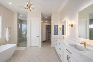 Full bath with double vanity, a stall shower, a freestanding bath, a walk in closet, and recessed lighting