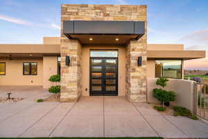Exterior entry at dusk featuring stone siding and stucco siding