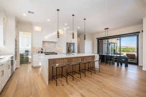 Kitchen featuring hanging light fixtures, decorative backsplash, a center island with sink, white cabinetry, and recessed lighting