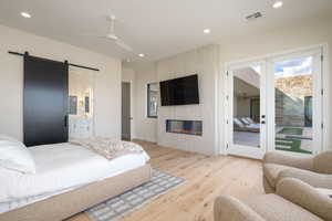 Bedroom with a barn door, light wood-type flooring, access to exterior, recessed lighting, and a ceiling fan