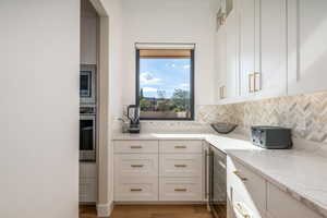 Kitchen with decorative backsplash, light stone counters, light wood-style flooring, white cabinets, and glass insert cabinets