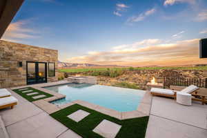 Pool at dusk featuring a mountain view, a pool with connected hot tub, and a patio