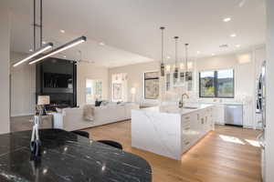 Kitchen with white cabinets, light stone counters, glass insert cabinets, a center island with sink, and recessed lighting