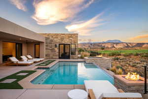 Pool at dusk with a mountain view, a patio, a pool with connected hot tub, and a fire pit