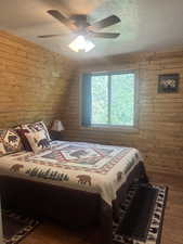 Bedroom featuring wood walls, wood finished floors, a textured ceiling, and a ceiling fan