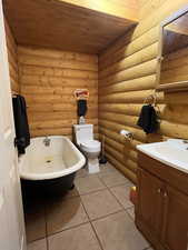 Full bathroom featuring vanity, a freestanding tub, wooden ceiling, light tile patterned floors, and log walls