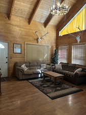 Living area with wood walls, high vaulted ceiling, a wood ceiling with exposed beams, a chandelier, and wood finished floors