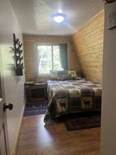 Bedroom with a textured ceiling, wooden walls, and wood finished floors