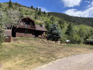 Rear view of property with a view of trees, a gambrel roof, faux log siding, a chimney, and a porch