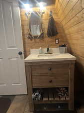Bathroom featuring wood walls, vanity, and vaulted ceiling