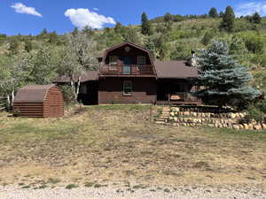 Rear view of house featuring a gambrel roof, a shed, covered porch, roof with shingles, and a forest view