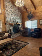 Living area with wooden walls, a wood ceiling with exposed beams, high vaulted ceiling, a fireplace, and wood finished floors