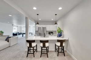 Kitchen featuring a peninsula, light colored carpet, white cabinetry, open floor plan, and a kitchen breakfast bar