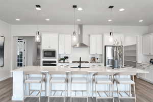 Kitchen with white cabinetry, tasteful backsplash, wall chimney range hood, hanging light fixtures, and light wood-style floors