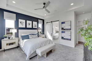 Carpeted bedroom with a barn door, a raised ceiling, multiple windows, and recessed lighting