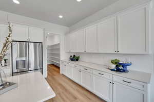 Kitchen with white cabinets, stainless steel fridge with ice dispenser, light wood-type flooring, recessed lighting, and decorative backsplash