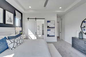 Bedroom with a barn door, carpet flooring, ceiling fan, a tray ceiling, and recessed lighting