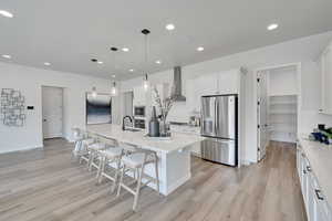 Kitchen featuring decorative light fixtures, stainless steel appliances, a breakfast bar, a kitchen island with sink, and white cabinetry