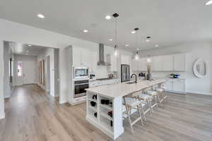 Kitchen with a breakfast bar area, decorative light fixtures, white cabinetry, recessed lighting, and a large island with sink