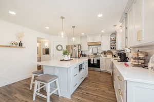 Kitchen featuring open shelves, stainless steel appliances, pendant lighting, a breakfast bar, and light stone counters