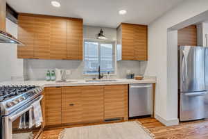 Kitchen with appliances with stainless steel finishes, light wood-style floors, decorative backsplash, wall chimney exhaust hood, and recessed lighting