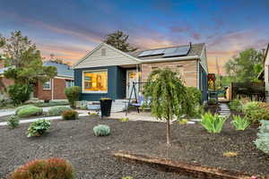 View of front of property with solar panels, brick siding, a patio, and a shingled roof