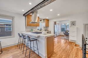 Kitchen featuring light countertops, light wood-type flooring, decorative backsplash, a breakfast bar, and recessed lighting