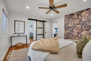 Bedroom featuring a barn door, wood finished floors, recessed lighting, a ceiling fan, and connected bathroom
