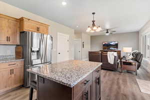 Kitchen with light stone counters, stainless steel fridge, pendant lighting, open floor plan, and recessed lighting
