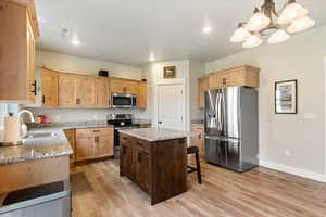 Kitchen featuring stainless steel appliances, light stone counters, light wood-style floors, a center island, and recessed lighting