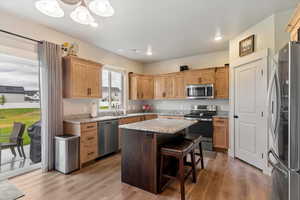 Kitchen featuring appliances with stainless steel finishes, light wood-style floors, light stone counters, a kitchen bar, and recessed lighting