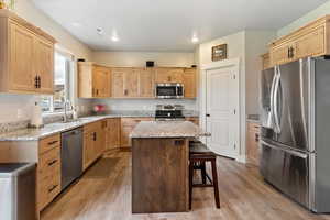 Kitchen with appliances with stainless steel finishes, light brown cabinetry, light stone counters, a kitchen island, and light wood-style floors