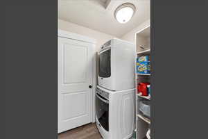 Washroom with light wood-style flooring and stacked washer / drying machine