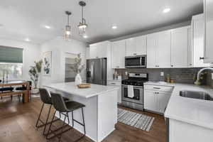 Kitchen with stainless steel appliances, white cabinetry, a kitchen island, hanging light fixtures, and a breakfast bar