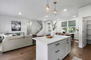 Kitchen with white cabinetry, engineering hardwood flooring, a center island, decorative light fixtures, and light stone countertops