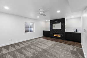 Downstairs living room with a fireplace, a ceiling fan, dark carpet, and recessed lighting