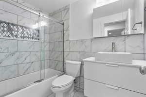 Basement full bath with vanity, shower / bath combination with glass door, tile walls, light marble finish floors, and a textured ceiling