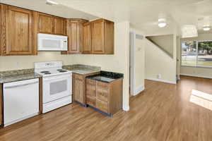 Kitchen with white appliances, brown cabinets, light wood finished floors, and dark stone countertops