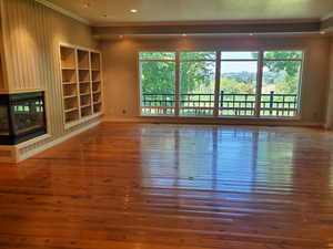 Unfurnished living room with a multi sided fireplace, wood-type flooring, ornamental molding, and recessed lighting