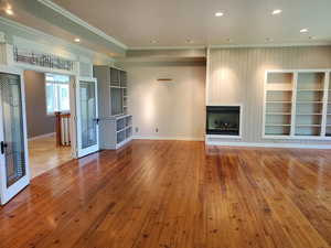 Unfurnished living room featuring recessed lighting, light wood-style floors, a large fireplace, ornamental molding, and built in shelves
