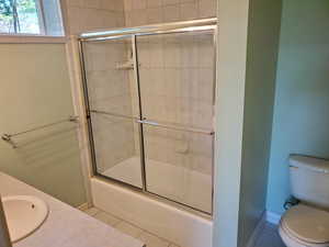 Full bath with bath / shower combo with glass door, tile patterned floors, and vanity