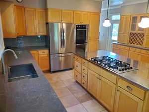 Kitchen with stainless steel appliances, tasteful backsplash, light tile patterned floors, ornamental molding, and light brown cabinetry