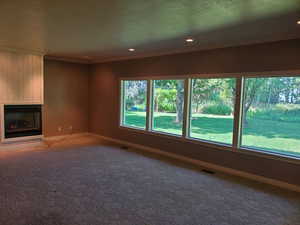 Unfurnished living room with a glass covered fireplace, crown molding, dark colored carpet, and recessed lighting