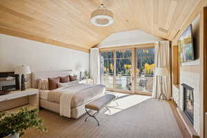 Bedroom featuring wood ceiling, a glass covered fireplace, access to exterior, and vaulted ceiling