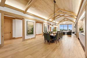 Dining area with light wood-style flooring, a wooden ceiling with exposed beams, a chandelier, and high vaulted ceiling