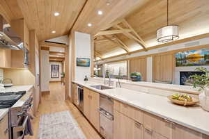 Kitchen featuring light brown cabinetry, decorative light fixtures, light wood finished floors, appliances with stainless steel finishes, and modern cabinets