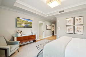 Bedroom featuring ornamental molding, light wood finished floors, and a tray ceiling