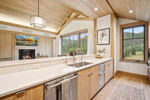 Kitchen with lofted ceiling, stainless steel dishwasher, light brown cabinets, decorative light fixtures, and light wood finished floors