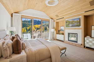 Bedroom featuring lofted ceiling, a tiled fireplace, wooden ceiling, access to exterior, and wood walls